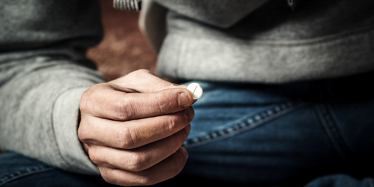 close up of pill being held representing a man needing help for drug and alcohol abuse