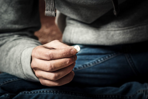 close up of pill being held representing a man needing help for drug and alcohol abuse