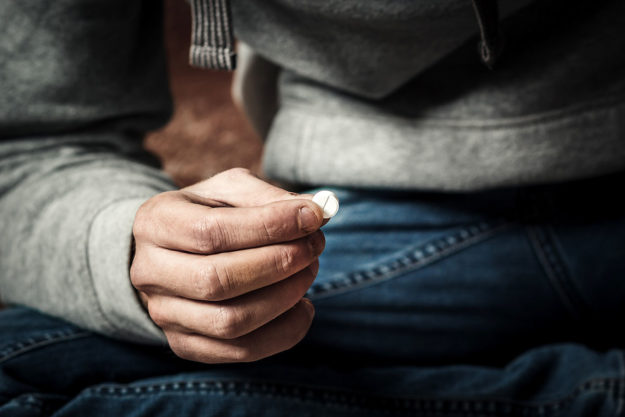 man sitting on the floor holding pill needing help preventing relapse after drug rehab