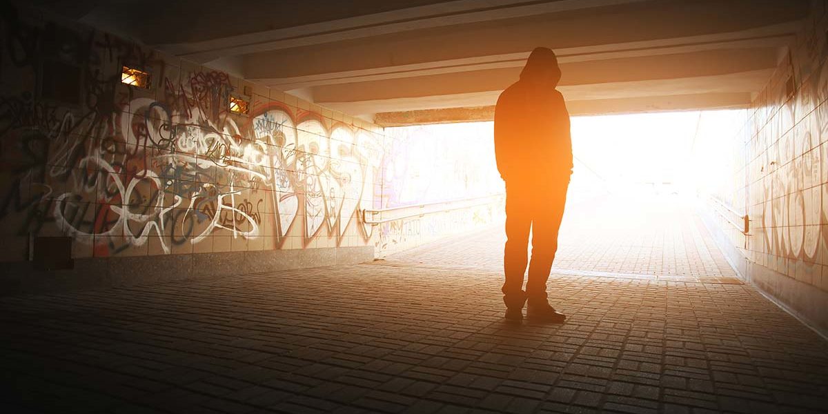 person turned toward the light outside of a graffitied tunnel representing drug recovery