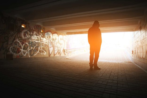 person turned toward the light outside of a graffitied tunnel representing drug recovery