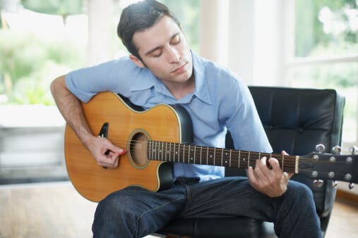 Man sitting in living room playing acoustic guitar