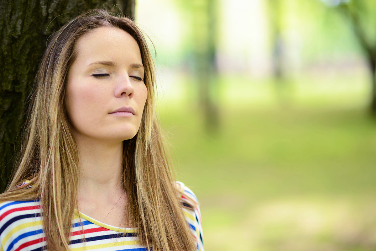 woman leaning against tree with eyes closed meditating on how to overcome addiction