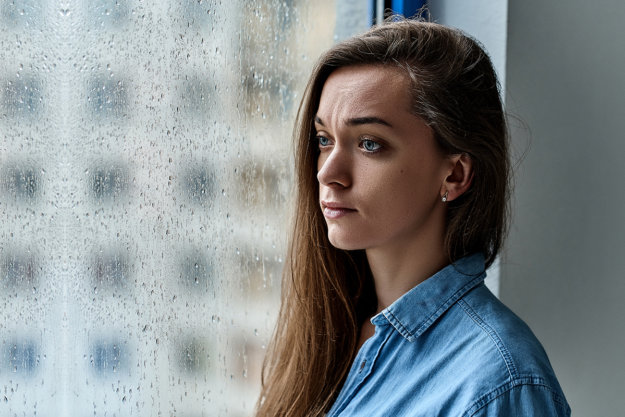 young woman looking out rainy window wondering is addiction a disease
