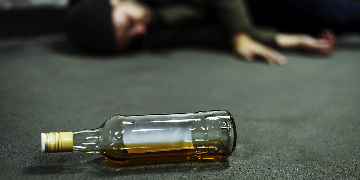 bottle of alcohol next to passed out man from drinking too much alcohol