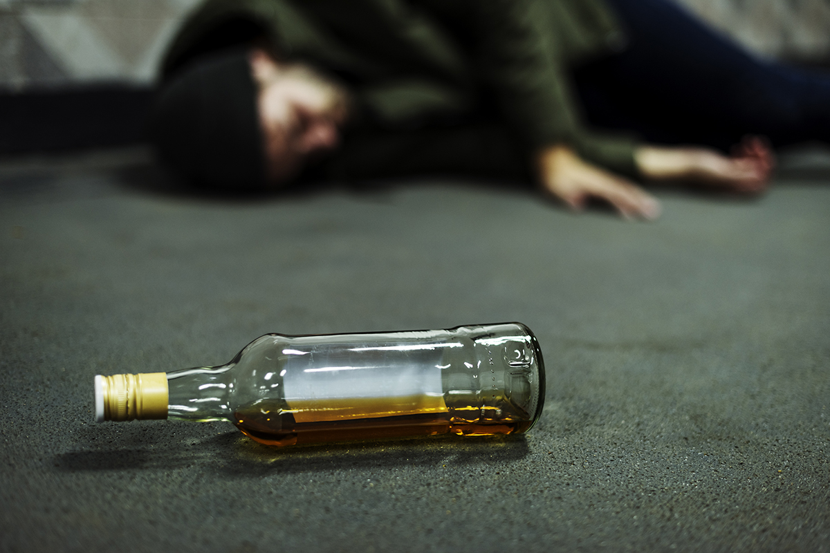 bottle of alcohol next to passed out man from drinking too much alcohol