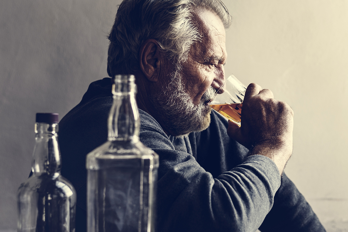 senior man sitting on floor heavily drinking in the stages of alcoholism