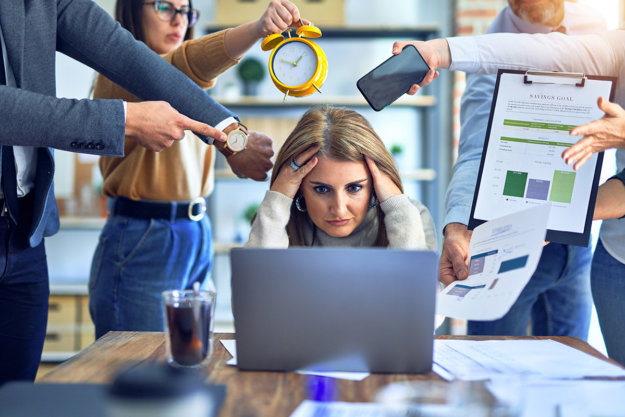 stressed woman at work surrounded by demanding coworkers knowing what causes alcoholism