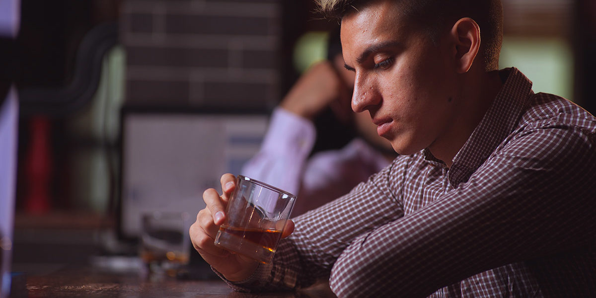 man at a bar staring into glass of alcohol wondering Am I An Alcoholic