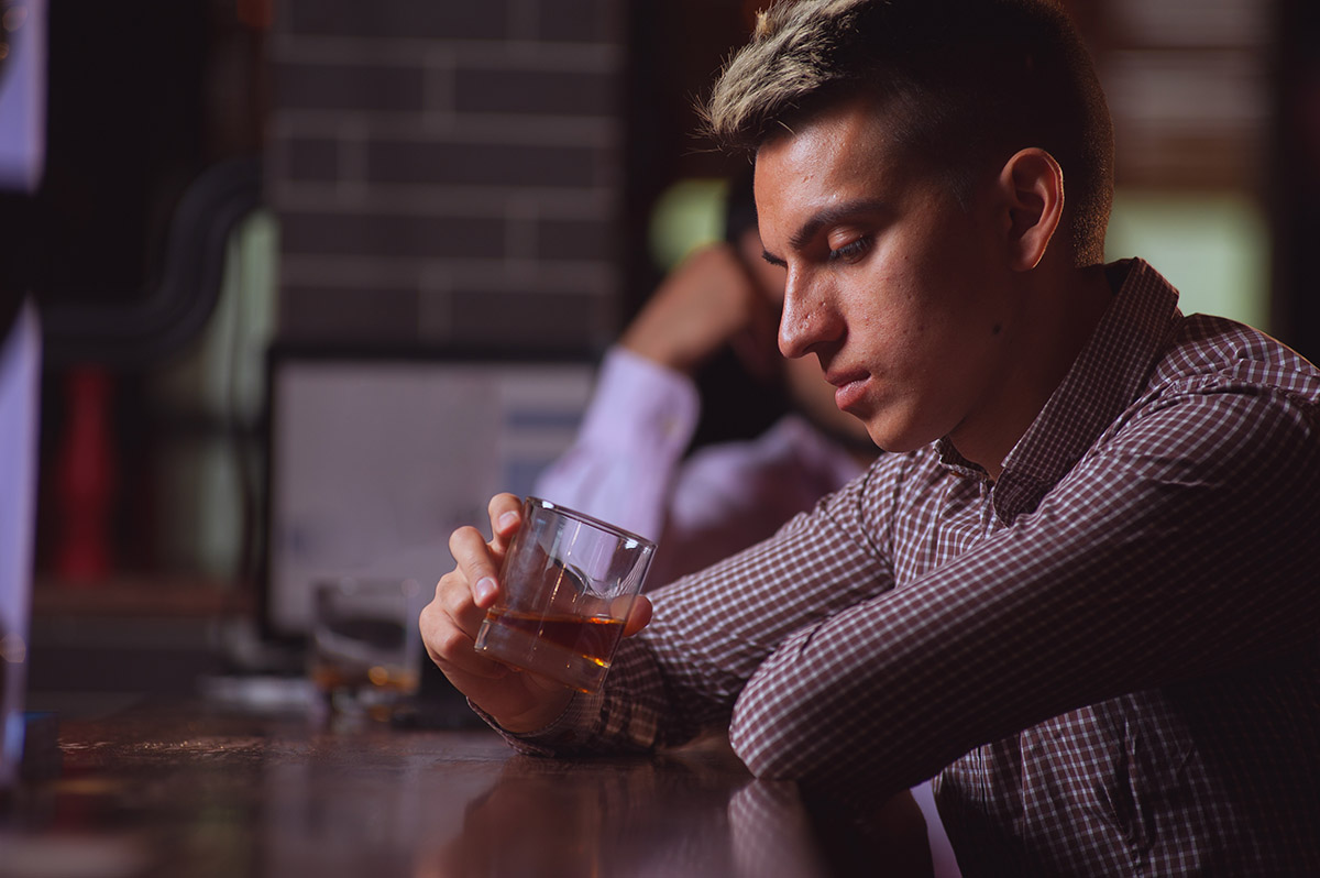 man at a bar staring into glass of alcohol wondering Am I An Alcoholic