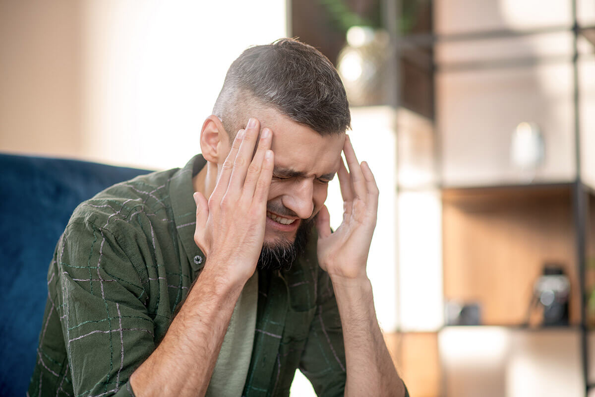 man in pain rubbing temples wondering how does alcohol affect the brain