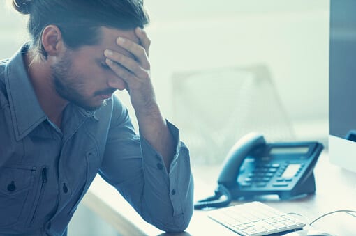 Man with hand on forehead at office desk experiencing drug side effects.