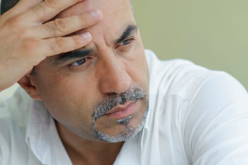 Man with grey beard holding head suffering detox symptoms.