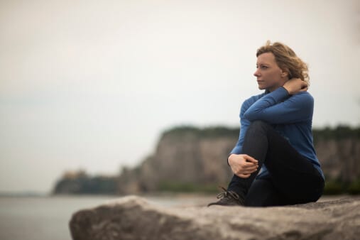 Woman on rock at water contemplating Florida sober houses for her continued recovery