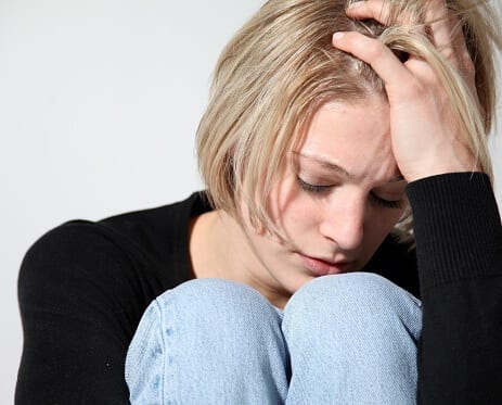 Blond woman curled up in distress over signs of cocaine withdrawal.