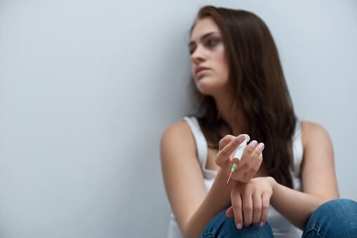 Using drugs by needle is the opiate definition for young woman against a wall.
