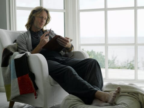 Man sitting comfortably in chair by window writing in journal at residential drug rehab center.