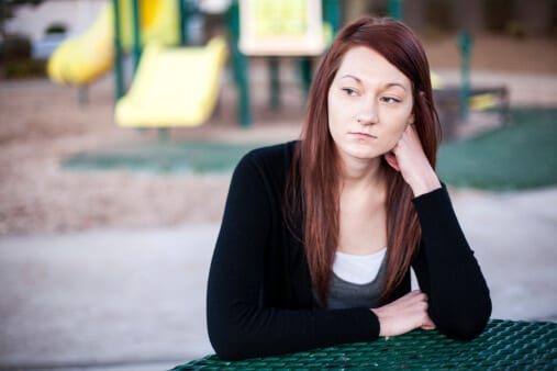 Sad woman with playground behind her worried about a kratom addiction.