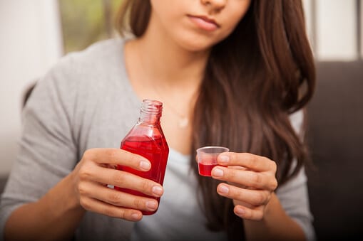 Young woman pouring cough syrup into a cup