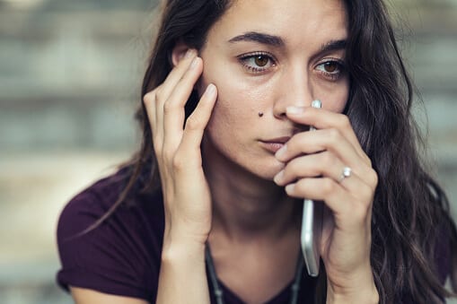 Sad woman with cell phone calling Beaches for addiction recovery.