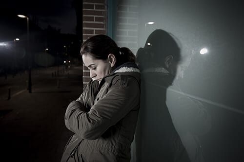 Despairing woman against wall in dark suffering with her meth addiction.