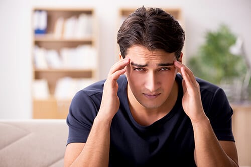 Young man with hands to temples noticing the physical dependence of drugs in headache.