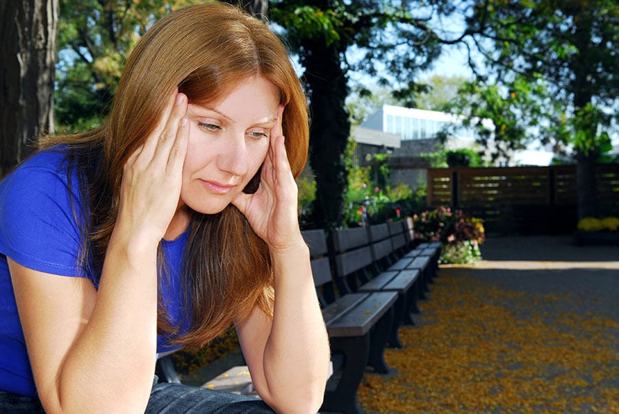 Woman with hands to temples wondering knows she needs alcoholic treatment for her addiction.