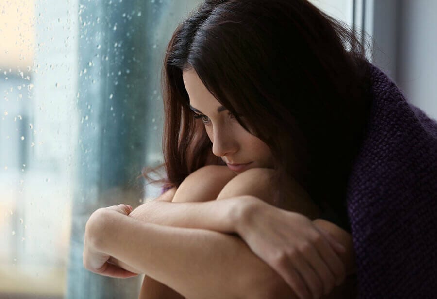 Woman curled up at rainy window contemplating her addiction and family codependency.