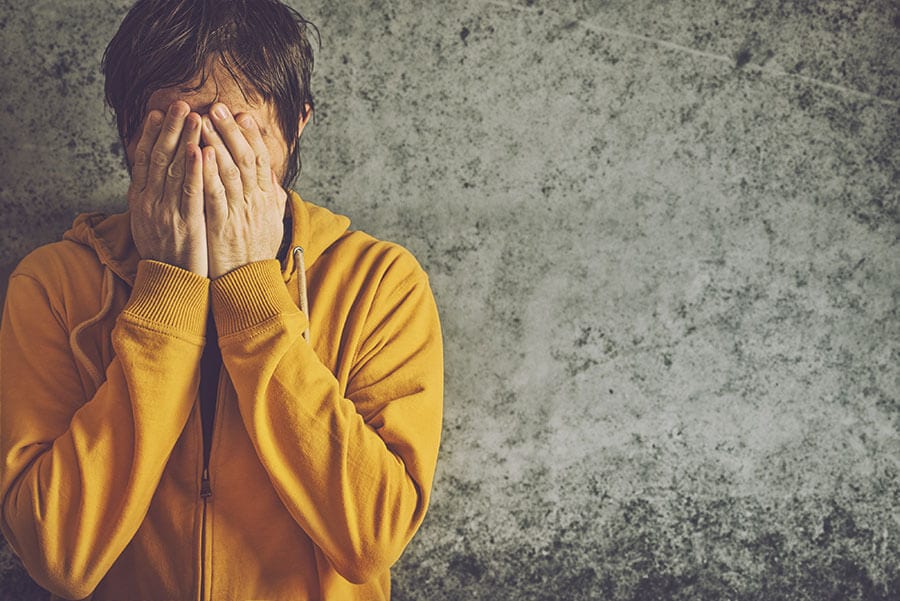 Man who needs heroin detox covering face in shame of heroin use