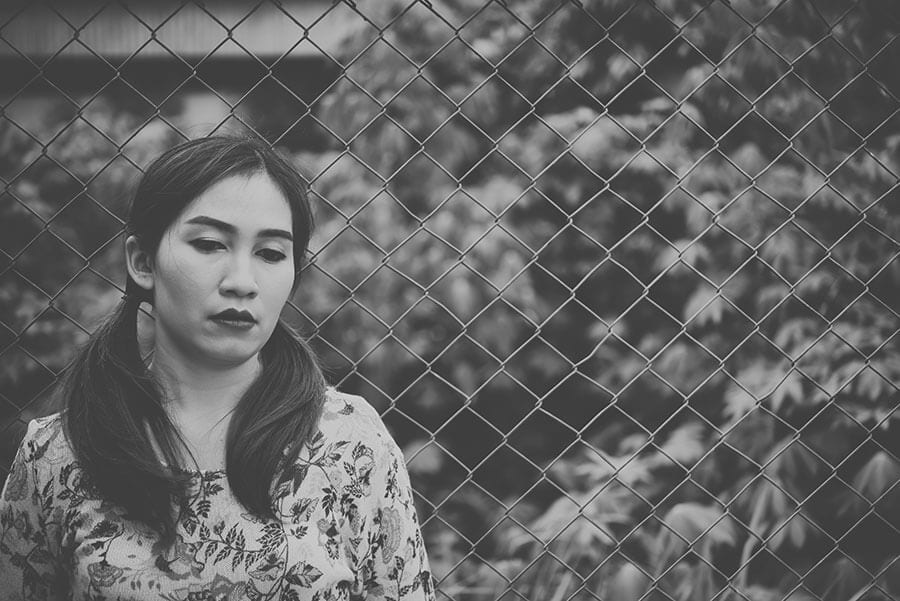 Sad alcoholic woman against fence wants to know, is alcohol a drug?