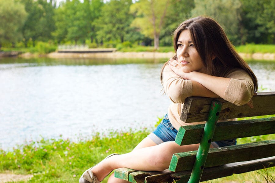 Woman on park bench at lake wondering if a NOVA recovery center will fill her need for rehab.