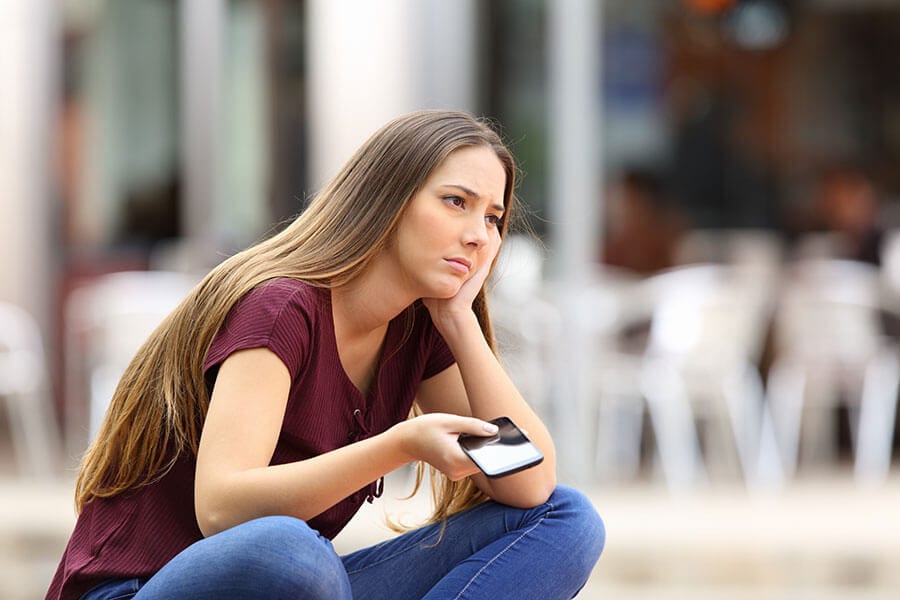 Sad long haired girl checks phone for prescription painkillers rehab help.