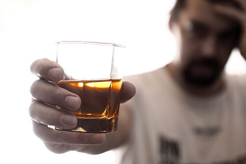 Man with headache lifting glass of booze may have an alcohol abuse disorder