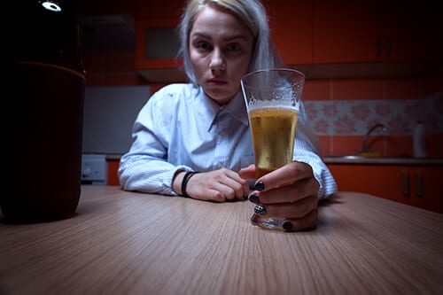 Drinking alone like this blond woman is part of the alcohol addiction definition