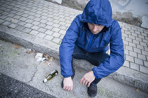 Man in blue jackets on a curb knows he needs alcohol addiction recovery