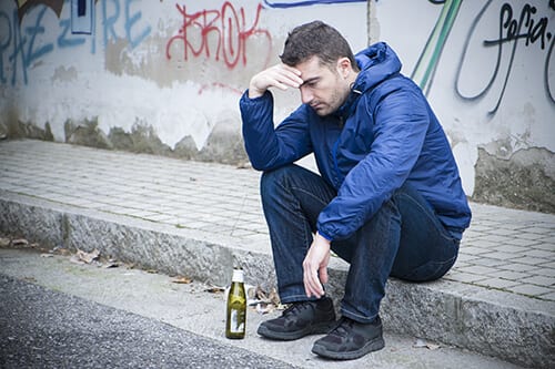 Man on curb with beer bottle adding to alcohol abuse statistics