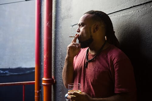 Man smoking against wall wonders if he may have a problem with alcohol and substance abuse