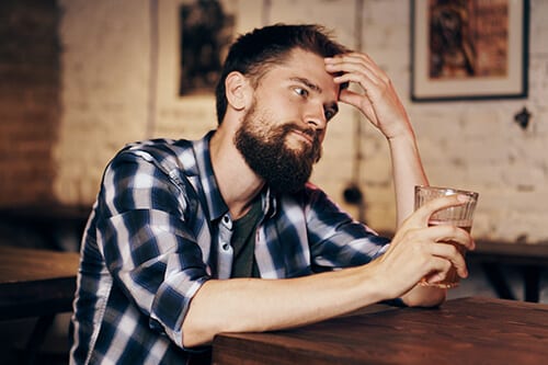 Bearded man at bar knows he needs to stop drinking but can't.