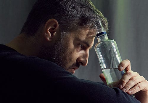 Depressed man holding bottle to head looking for alcoholism treatment program