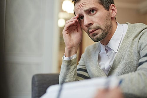 Sad looking man with hand to head struggling through cognitive behavioral therapy for addiction.