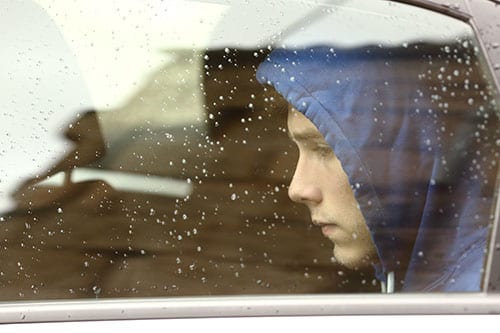 Boy behind rainy window depressed about admitting to being a meth addict.