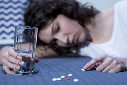 Young woman on blue bedspread counting out her pill addiction.