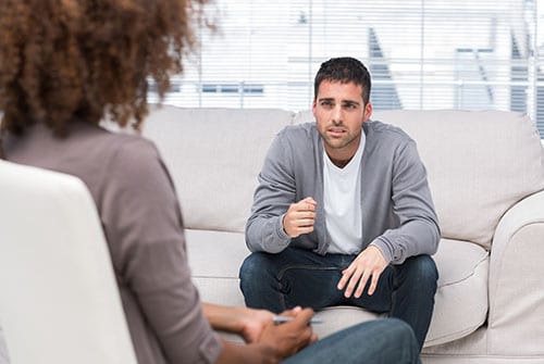 Man on couch talking to a therapist during rehab counseling.