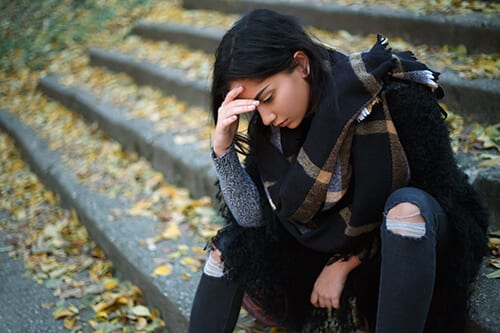 Young woman in ripped jeans on cement stairs knows she has opioid addiction signs.