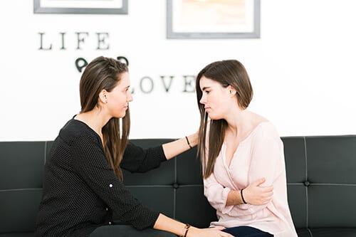 Two women on a sofa helping each other during rehab treatment.