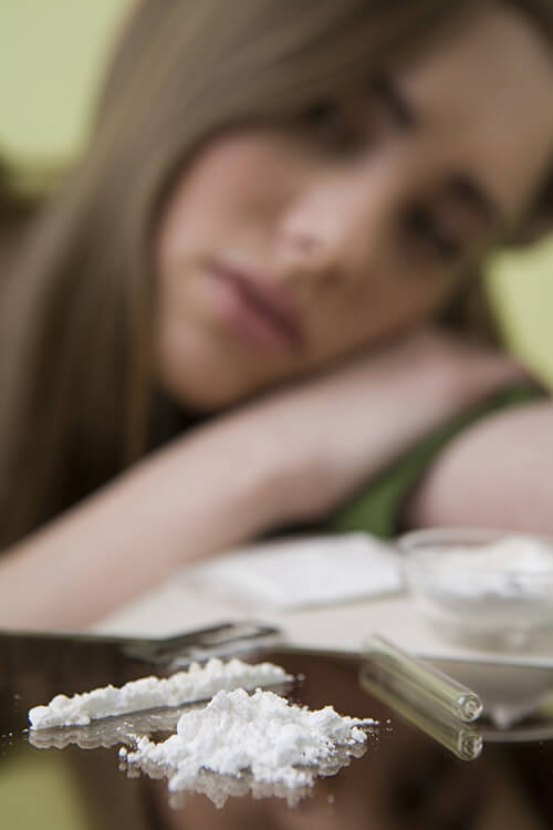 Young woman out of focus in background, cocaine relapse right in the foreground.