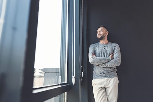 Bearded man gazing out window of a heroin detox center.