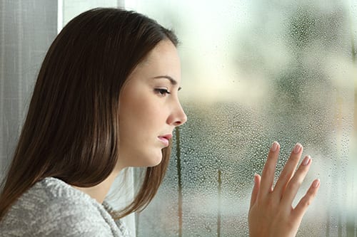 Sad young woman at rainy window knows how to define substance abuse for herself.