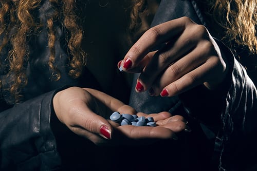 Manicured hands holding pills that will lead to opioid addiction symptoms.