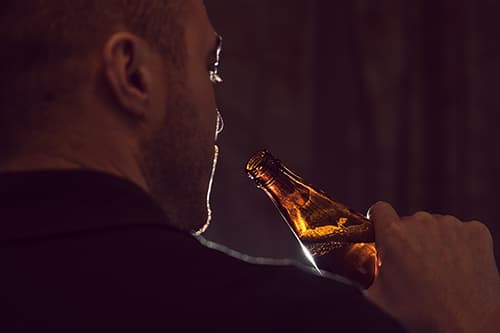 Man in dark drinking may not realize his alcohol dependence symptoms.